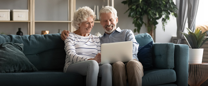freundliches, älteres Ehepaar auf Couch mit Laptop